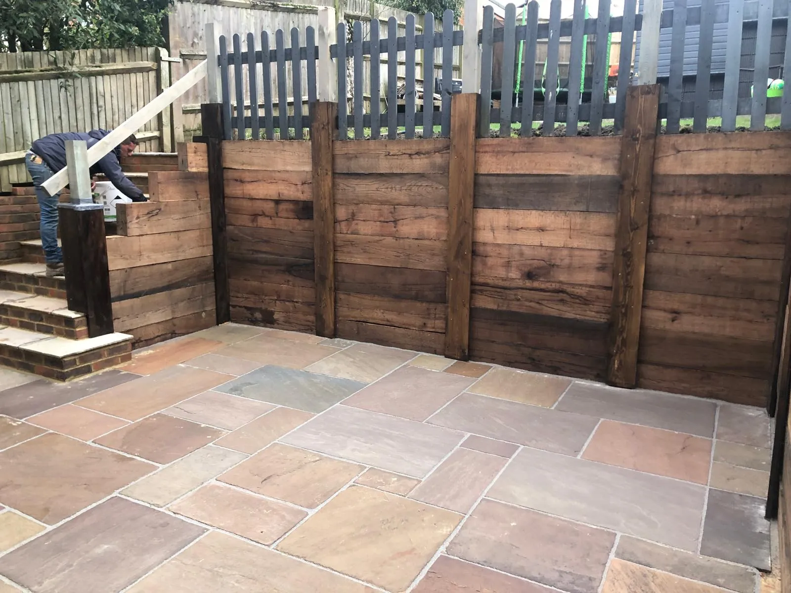 Sleeper patio: Sandstone patio with a railway sleeper retaining wall and steps up to the lawn.