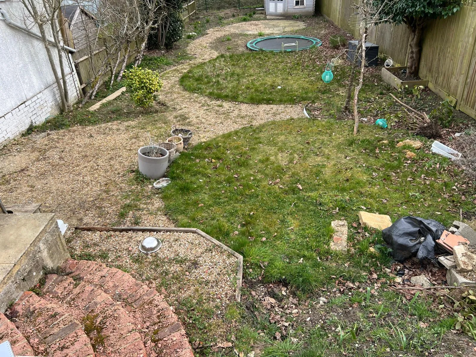 Patchy lawn and loose gravel, with the trampoline sitting proud of the ground.