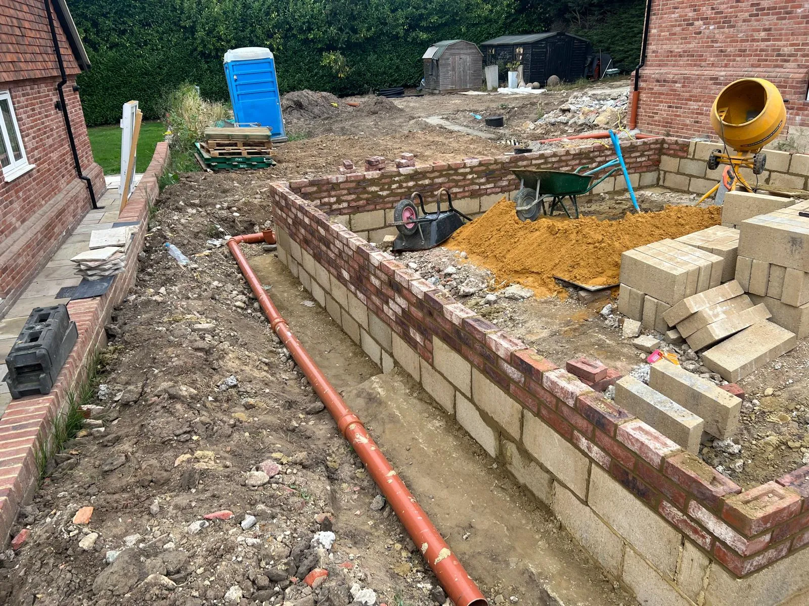 Brick face laid against the block, with a drainage pipe in the trench.