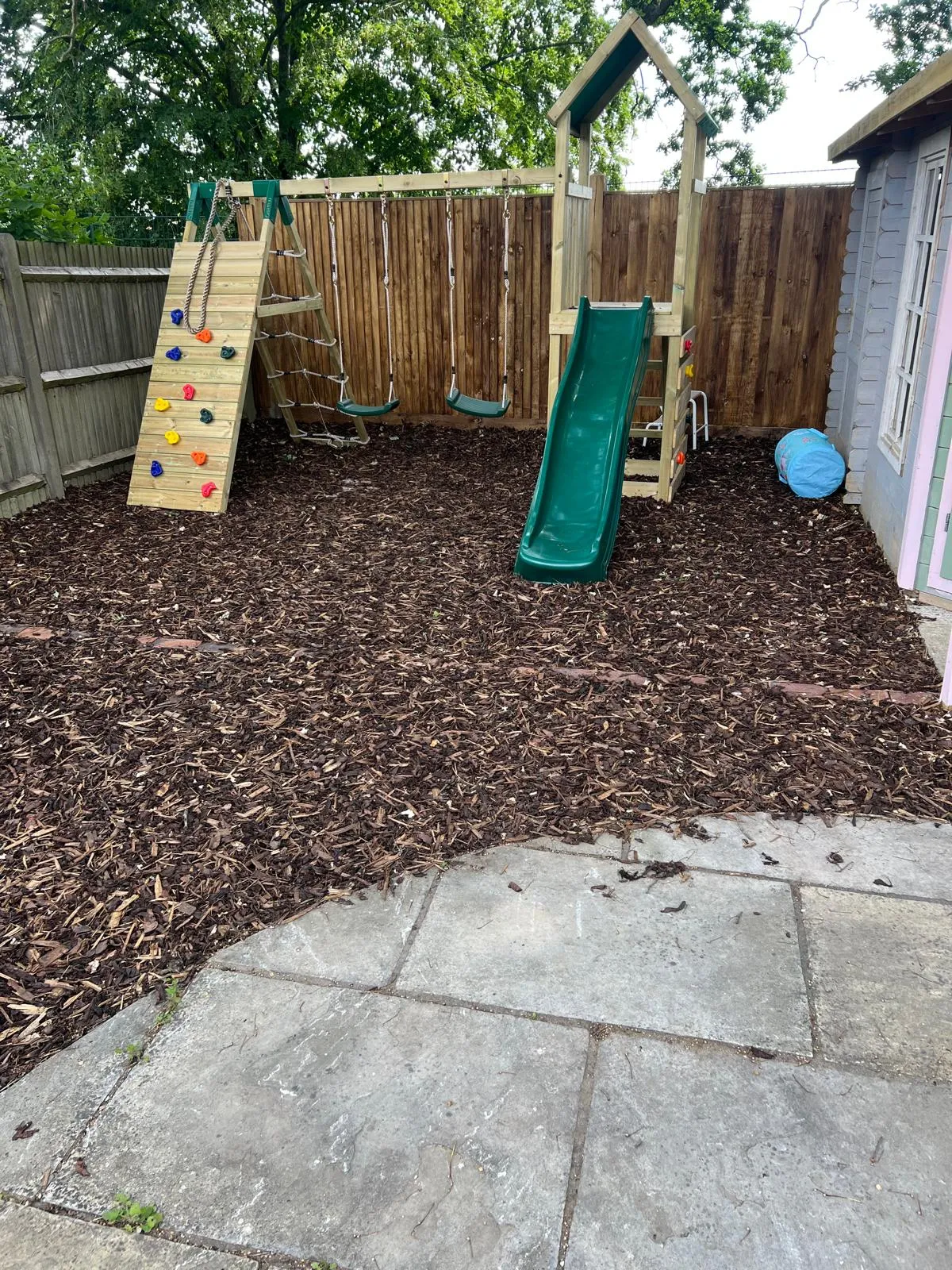 Bark play area with a climbing frame, edged in brick.
